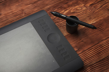 Part  graphic tablet and pen  lie on a brown wooden background