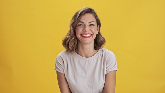 Pretty young woman with red lips laughing and applauding while looking at the camera over yellow background isolated                                                                