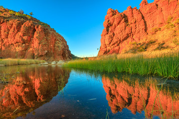 Scenic red rock formations of Glen Helen Gorge of West MacDonnell Ranges mirroring on calm waters...