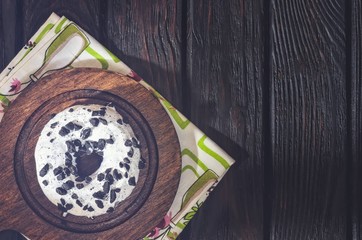 Delicious sweet snack served in a vintage style. Donut with a hole in white topping on dark wood.