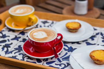 Two Cups of coffee latte in ceramic cups with traditional Portuguese dessert pastel de nata. Top view, food, menu concept. Latte art coffee with sweets on a tray