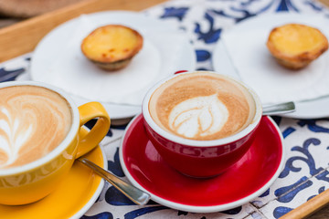 Two Cups of coffee latte in ceramic cups with traditional Portuguese dessert pastel de nata. Top view, food, menu concept. Latte art coffee with sweets on a tray