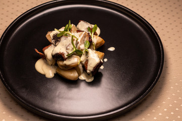 Deer heart with porcini mushrooms and sauce on a black plate.