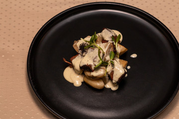 Deer heart with porcini mushrooms and sauce on a black plate.