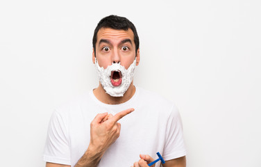 Man shaving his beard over isolated white background surprised and pointing side