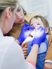 Childrens dentistry. Dental examination. Dentist treats the boys teeth. Female dentist treats teeth. Boy 0-1 age. Oral health.