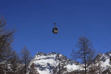 Gondola passing in front of alpine snow mountains and blue sky.