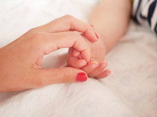Mom holds the hand of a newborn baby. Close-up. A place to write. Placing text. defocusing. Baby's hand holding finger to mom.