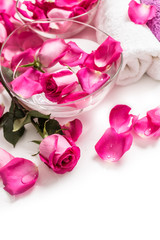 Pink roses petals in bowl with towels and pure water over white.. Spa and wellness concept