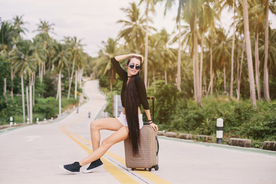 Beautiful style girl seating with suitcase on tropical road