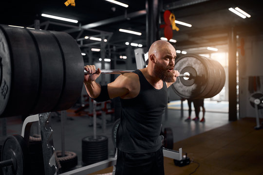 Strong active powerlifter attempting to lift heavy barbell row, standing near metal bar, looking away with serious face and opened mouth, making effort, workout concept, portrait