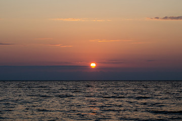 The bright red sun sets over the sea horizon