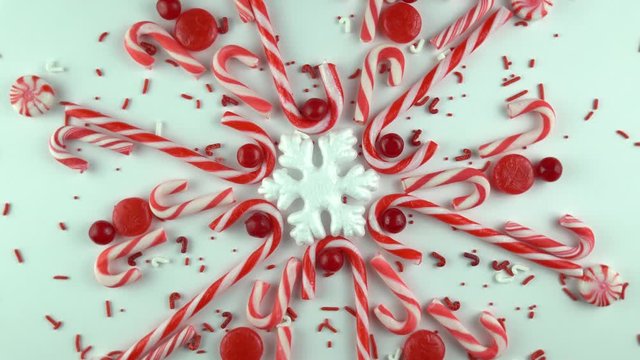 Traditional Christmas day, red snowflake made of peppermint candy cane rotating or spinning seamless in the loop. Slow motion of cinnamon lollipop sweets and sprinkles arranged kaleidoscope.