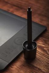 Part of graphic tablet and pen  lie on a brown wooden background