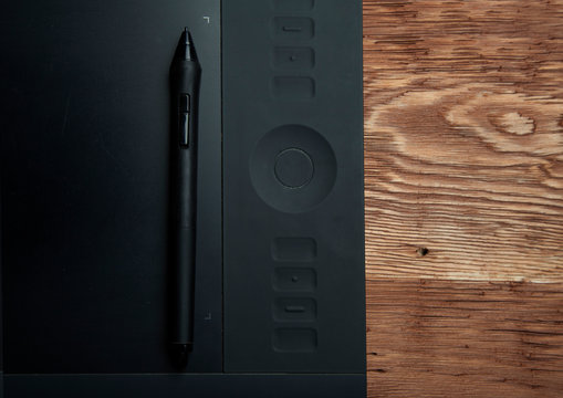 Part of graphic tablet and pen  lie on a brown wooden background photo