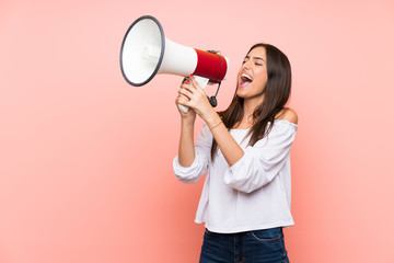 Young woman over isolated pink background shouting through a megaphone