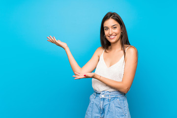 Young woman over isolated blue background extending hands to the side for inviting to come