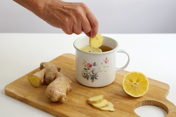 Closeup shot of ginger and ginger tea with lemon in the decorative container - woman's hand holding ginger
