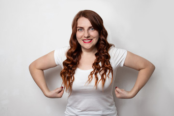 Female power. Young red-haired young woman, showing muscles, trying to look dangerous, smiling and standing on a gray background.