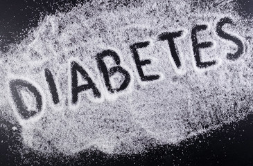 The word DIABETES on the spilled sugar on black background. Harm of sugar, diabetes disease medical concept.