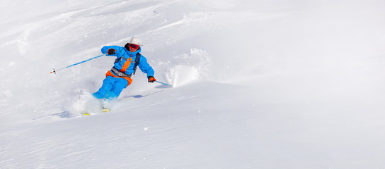 Skier skiing downhill in high mountains. professional rider in bright blue-orange ski suit and original hat on his head. snow-white background and place for text editing. Epic free ride scene