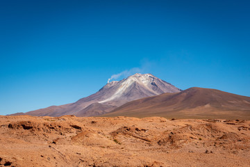 At the edge of Reserva Nacional de Fauna Andina Eduardo Avaroa, Putana Volcano lies on the border of Bolivia and Chile. Smoke streams from its crater flowing into the clear blue sky above.