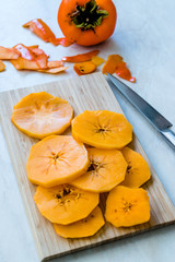 Sliced Persimmon Fruit Slices on Wooden Board with Knife.