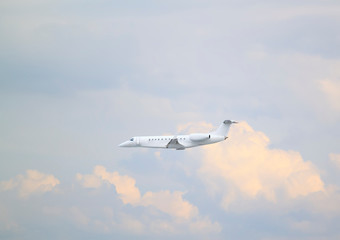 White private jet business jet flies against backdrop of beautiful white clouds on blue sky