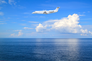 Fototapeta na wymiar Private spy jet business plane flies low over sea of background of beautiful calm seascape with white clouds