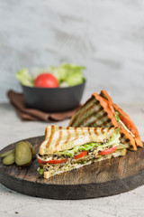 Fresh tuna, tomato, pickle and lettuce sandwich on bread toast closeup on wooden Board.