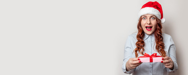 Young curly girl with santa hat, green sweater with gift boxe in her hands on a gray background. Merry Christmas and New Year web banner for site. Christmas shopping day