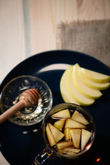 Tea with honey and sliced apples. Top view of cup, black plate and wooden spoon.