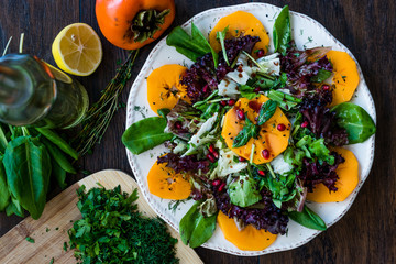 Persimmon Fruit Salad with Pomegranate, Lollo Rosso Lettuce, Rocket Arugula or Rucola and Mint Leaves.