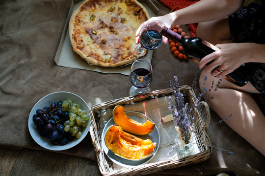  Top view of pizza slices and grapes on the floor.Woman pours wine into a glass.