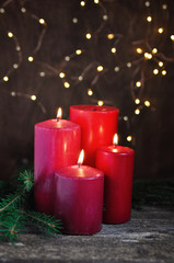 Four Red candles and tree branches for Christmas and new year on retro wooden table and garland lights background.