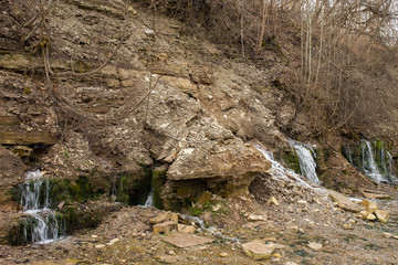 Natural textures. The spring flows from a steep rocky hillside. Early spring. Izborsk, Pskov region, Russia.