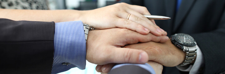 Focus on businesspeople putting hands on top of each other. Colleagues celebrating of signing profitable contract. Teamwork concept. Blurred background