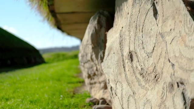 hand held close shot of ancient engravings on Boyne valley tombs stone wall in Knowth. Prehistoric circular patterns of religious astrological and ritual meaning in the warm irish sun on and blue sky
