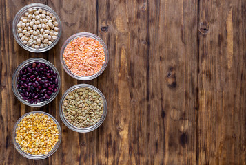 Various legumes in bowls on a wooden background.