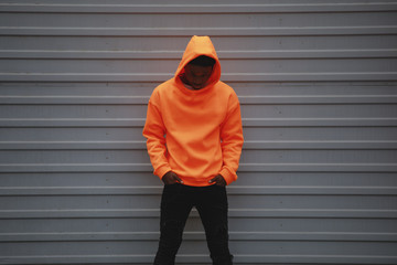 African American man wearing blank orange hoodie standing against grey wall