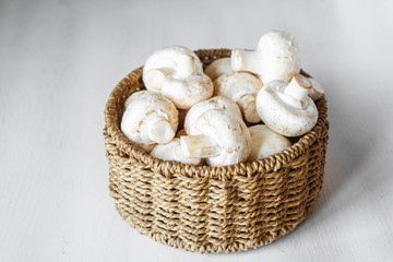 Fototapeta na wymiar Mushrooms champignons in a round wicker basket on a white wooden table. Place for text or advertising