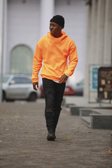 Handsome African man model wearing bright orange hoodie in city