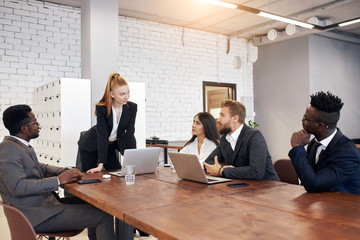 American woman in formal wear explain strategies to caucasian and african people. Office background