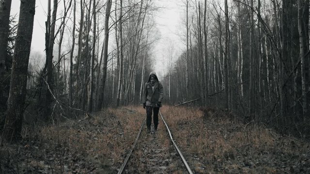 Wanderer man in gas mask walking on old abandoned railway in empty dead forest. Apocalypse concept, male stalker survivor after nuclear or chemical disaster. Post apocalyptic world