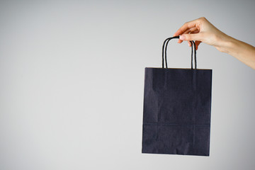 Black friday concept. Paper blue craft bag, eco packaging in a female hand, on a gray background....