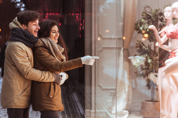 Couple Standing Outdoor Of A Store Pointing Finger At Shopwindow