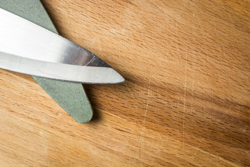 Scratched kitchen knife for vegetables with grindstone made of coarse abrasive on wooden board.