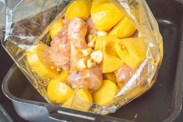 Raw chicken legs and sliced potatoes in roasting bag in oven.
