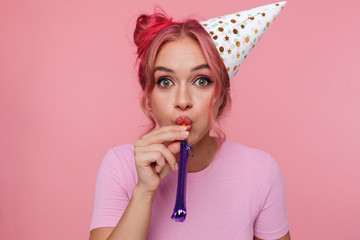 Portrait of happy woman wearing party cone blowing in whistle