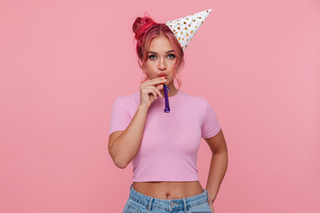 Portrait of young woman wearing party cone blowing in whistle